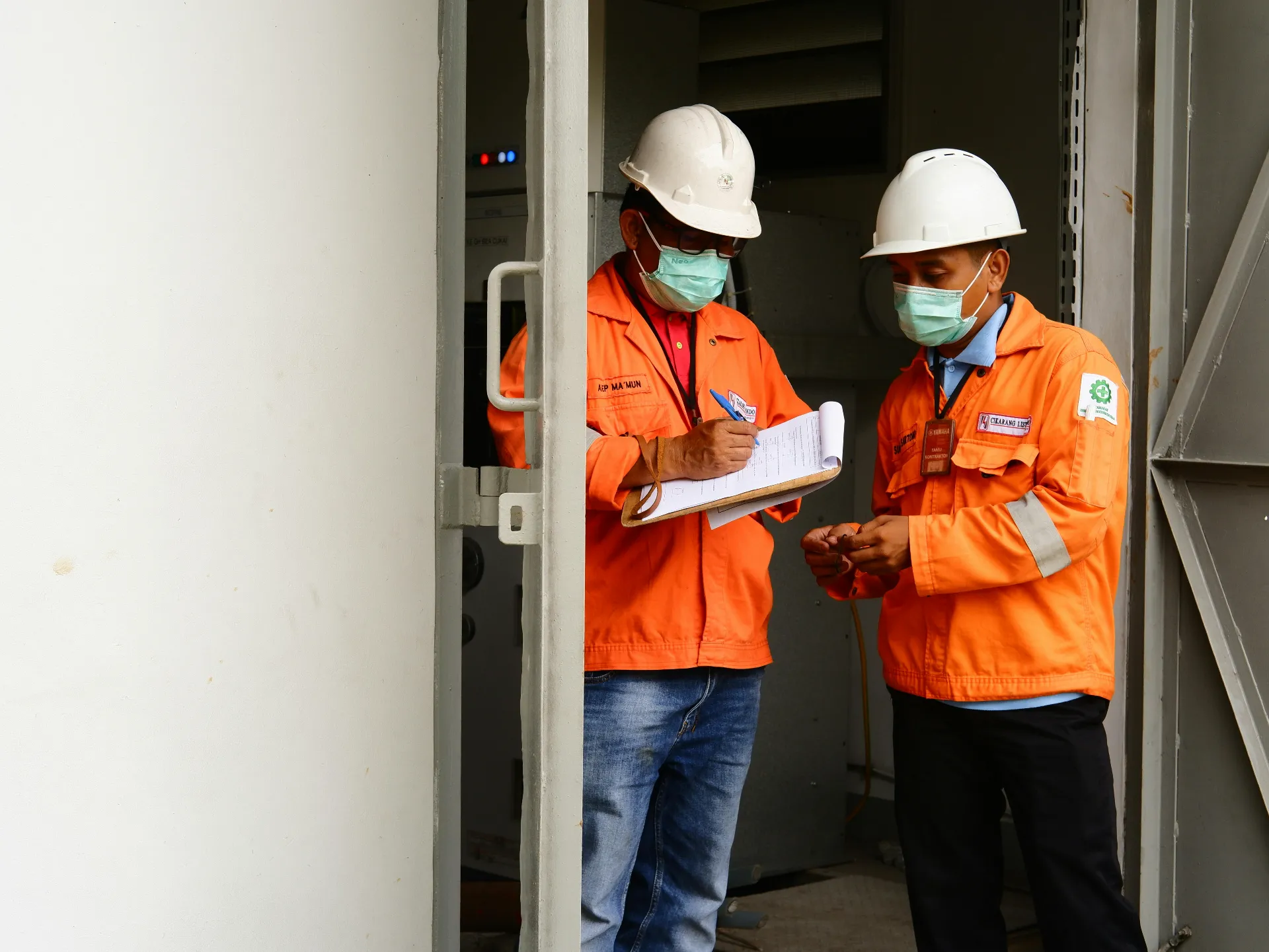 Men in orange jackets and hard hats reviewing H2S certification on a clipboard
